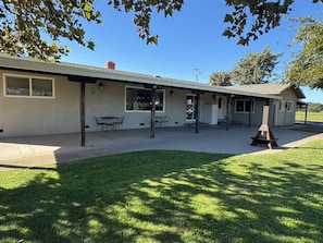A single-story building with a covered patio area, a small outdoor seating arrangement, and a grassy lawn.