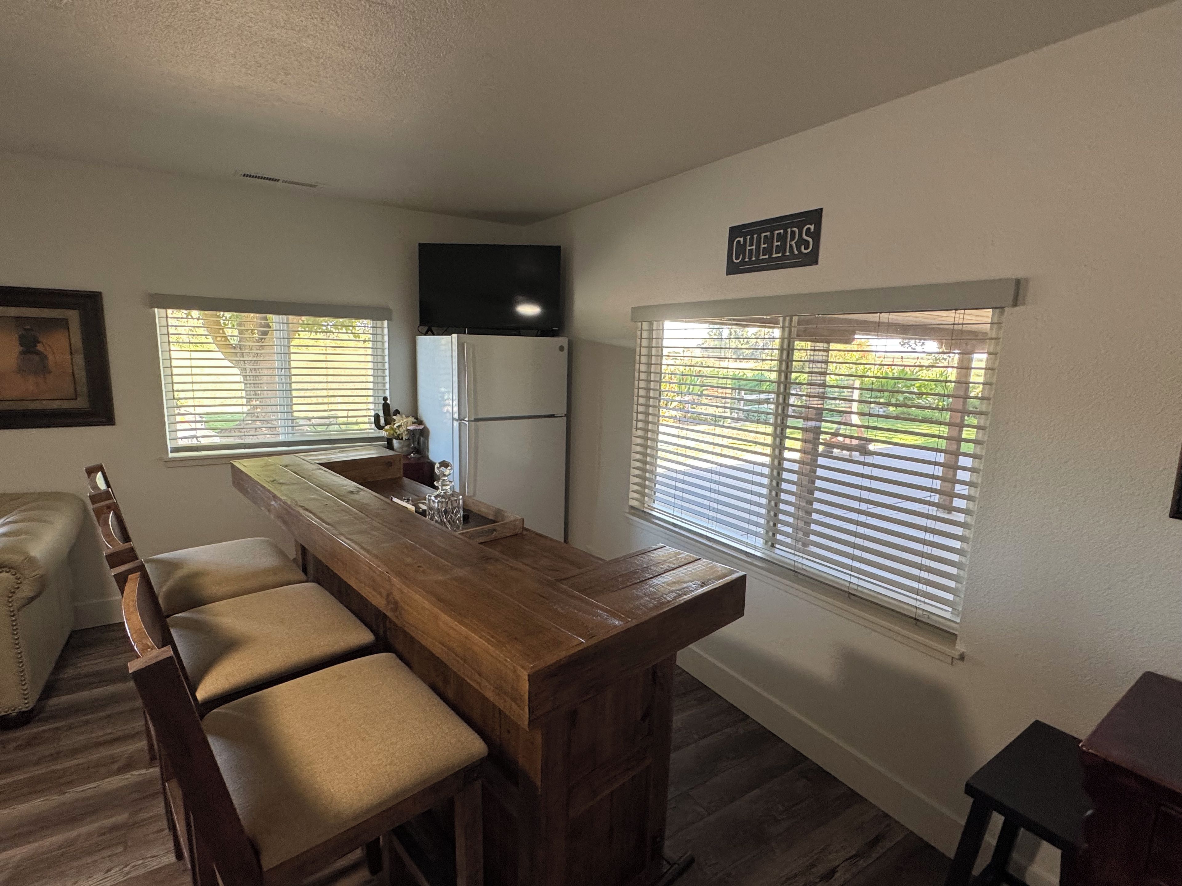 A kitchen with a wooden bar, a refrigerator, and a sign that says 'CHEERS'.