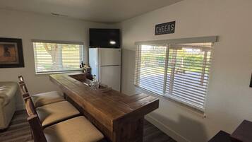 A kitchen with a wooden bar, a refrigerator, and a sign that says 'CHEERS'.