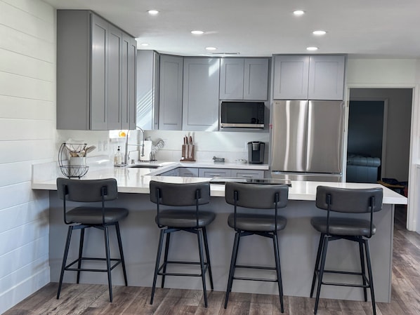 A modern kitchen with grey cabinets, stainless steel appliances, and a central island with bar stools.