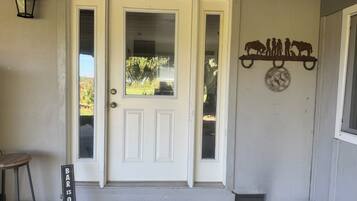 A white front door with a glass panel, a black bar sign, a metal horse decoration, and a small stool.