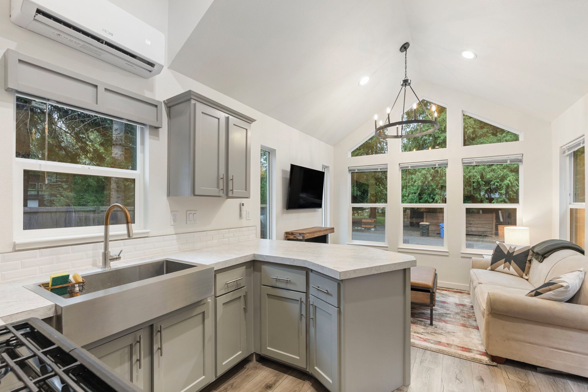 A modern kitchen with a large island, grey cabinetry, and a built-in TV.