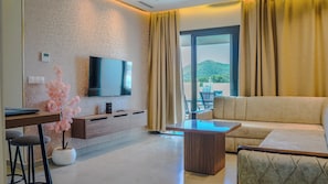 Une chambre d’hôtel moderne équipée d’un téléviseur à écran plat fixé au mur, d’un canapé, d’une table basse et d’un coin repas comprenant une chaise et une petite table.