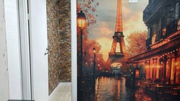 A room with a large mural of the Eiffel Tower, a brick wall, a wooden floor, and a television.