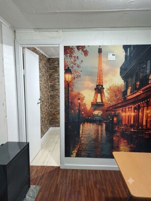 A room with a large mural of the Eiffel Tower, a brick wall, a wooden floor, and a television.