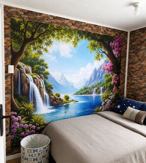 A bedroom with a mural of a waterfall and mountains, a bed with a star-patterned pillow, and a trash can. - Sinchi Warmi 1 - Cozy & Central in Patagonia (Punta Arenas)