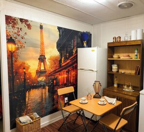 A room with a dining table, chairs, a refrigerator, and a shelf with kitchen items. - Sinchi Warmi 1 - Cozy & Central in Patagonia (Punta Arenas)