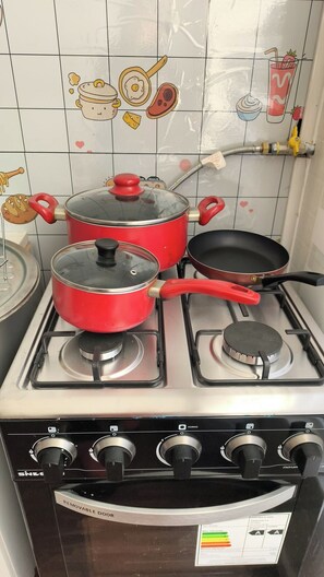 Cuina amb fogó de gas, dues olles vermelles, una paella i un robinet.
