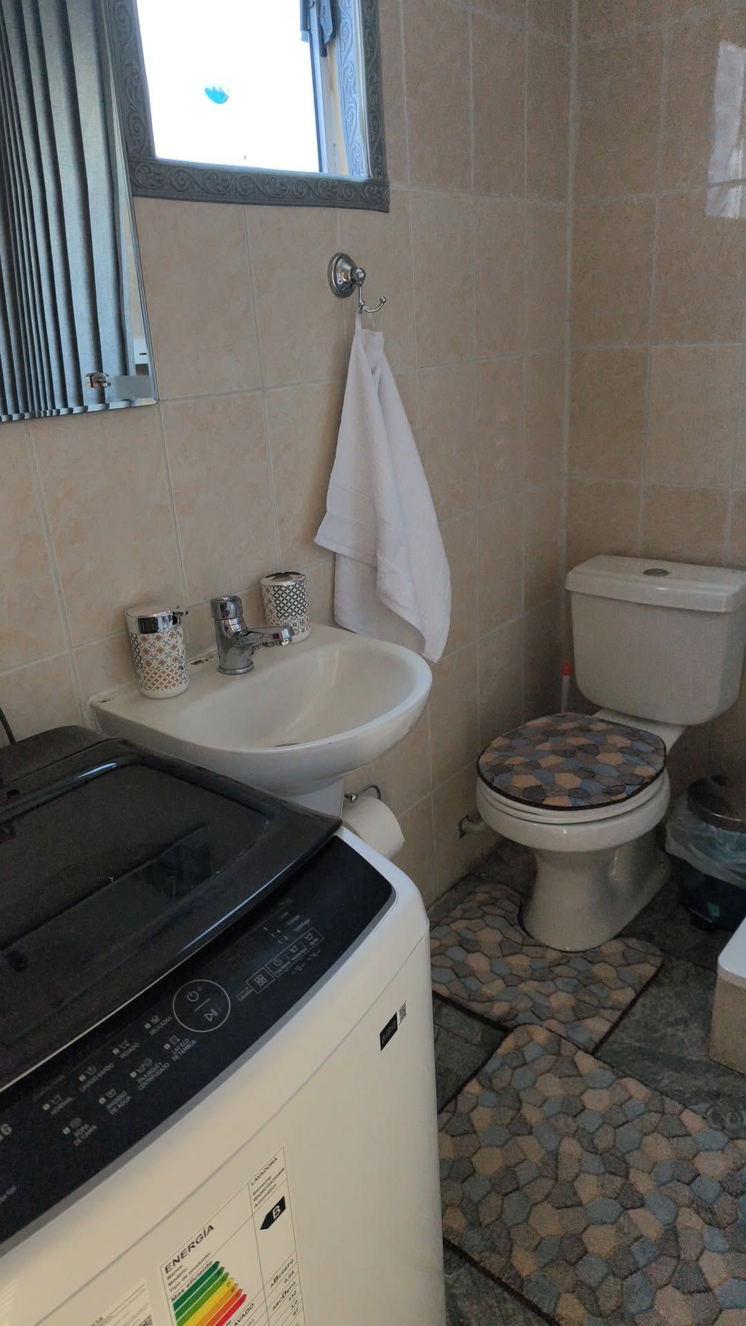 Un bagno piccolo ma funzionale, dotato di lavatrice, lavandino, wc e finestra con tende.