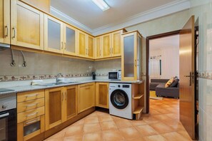 A compact kitchen with wooden cabinets, a washing machine, and a microwave. - Brisa do Tejo, By Home Match (Alcochete)