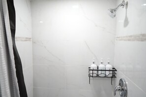 Ein Badezimmer mit Dusche, einer Marmorwand und Ablage für Toilettenartikel.