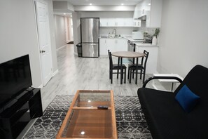 A modern living room with a black sofa, a glass coffee table, and a TV. - Cozy Basement Suite in Brampton | Modern & Central (Brampton)