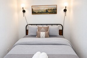 Ein Bett mit grauer Bettdecke, mehreren Kissen und zwei Wandleuchten.