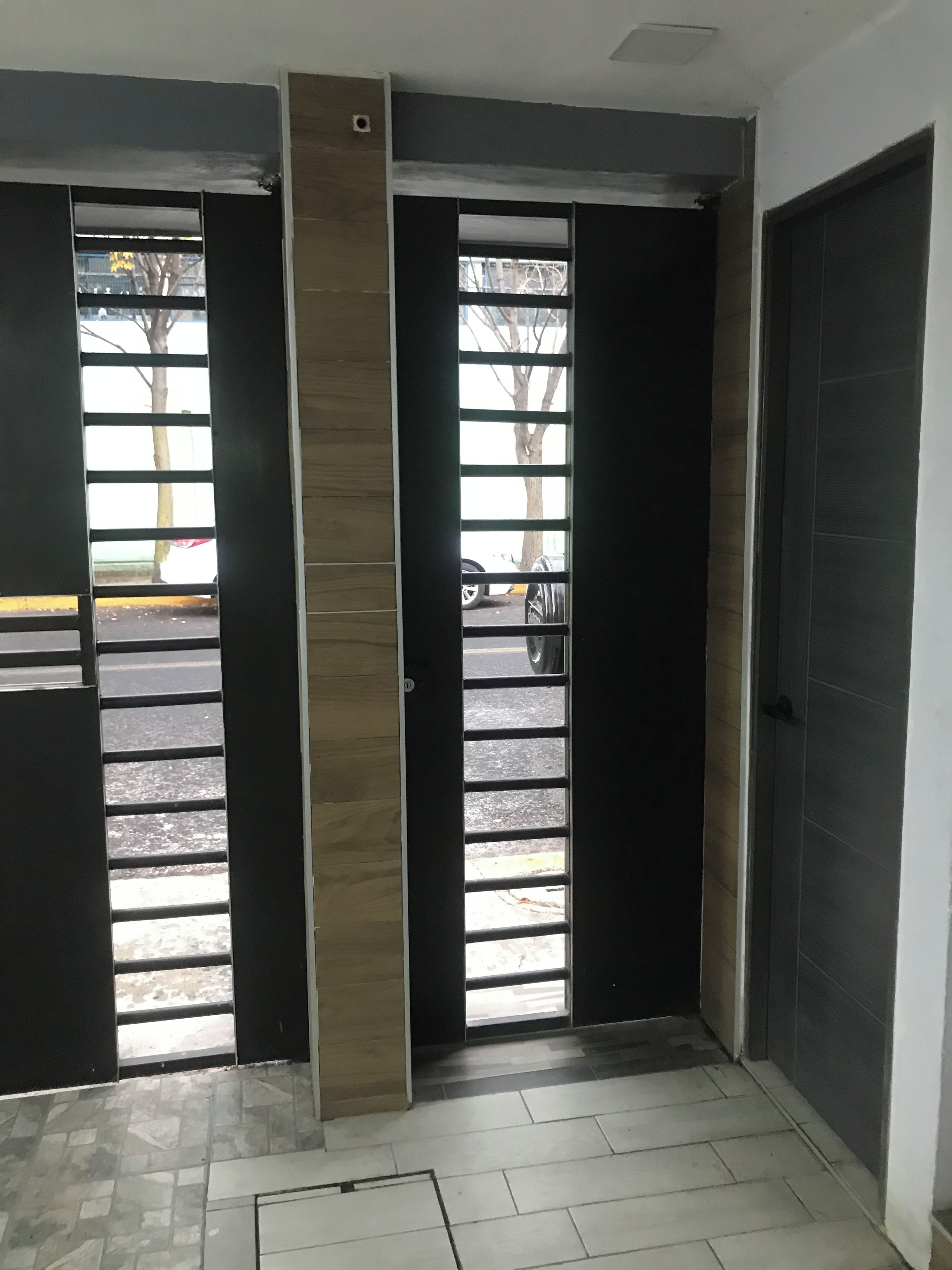 Un pasillo con piso de baldosas, una puerta con manija de metal y vista a la calle.