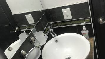 Un baño con un lavamanos blanco, un espejo, un perchero para toallas y una botella de jabón.