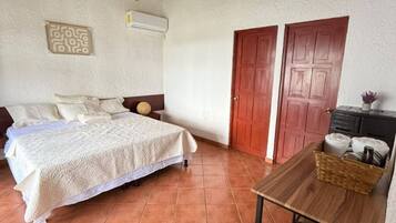 A bedroom with a bed, a wooden table, a chair, a wardrobe, and a ceiling with wooden beams.