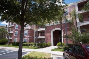 A multi-story residential building with a central entrance, balconies, and a parking lot. - 7-305 3 Bedroom Condo (Orlando)
