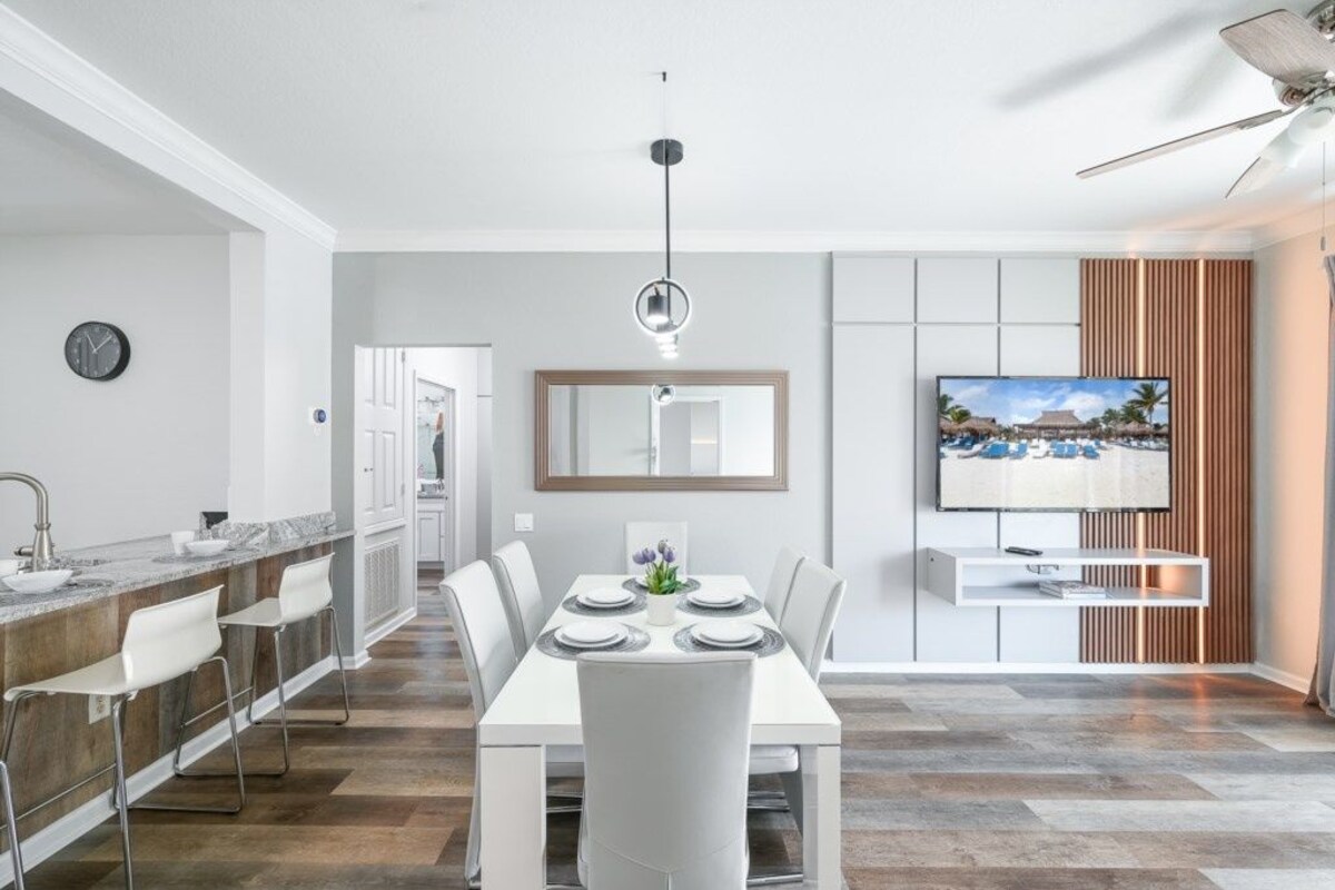 A modern kitchen with a dining area, a TV mounted on the wall, and a ceiling fan.