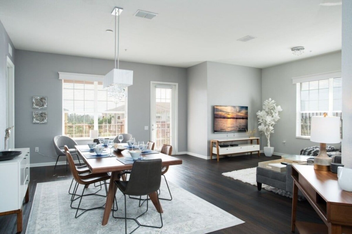 A modern living room with a dining area, a flat-screen TV, and a large window.