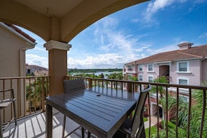 A balcony with a table and chairs, overlooking a body of water and neighboring buildings. - 7-305 3 Bedroom Condo (Orlando)