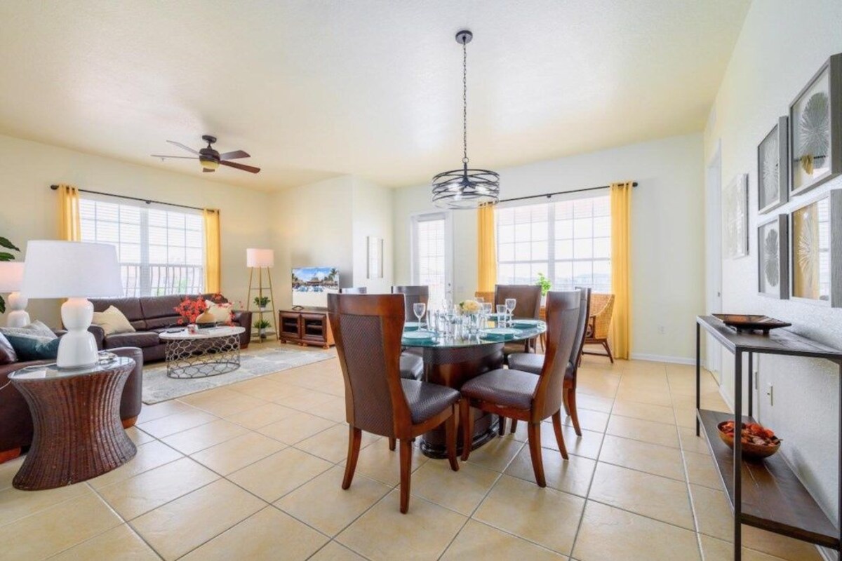 A spacious living room with a dining area, large windows, and a ceiling fan.