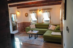 A living room with a green sofa, a small table, and a brick fireplace. - Imanje brodara Tome - Hot Tub, Garden, WiFi (Lekenik)
