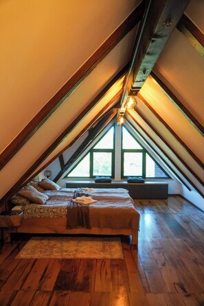 A loft bedroom with a sloped ceiling, wooden beams, a bed with pillows, a rug, and a window with a view. - Imanje brodara Tome - Hot Tub, Garden, WiFi (Lekenik)