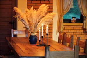 Une table de salle à manger en bois, ornée d’un vase contenant des herbes des pampas séchées et de trois bougies allumées.