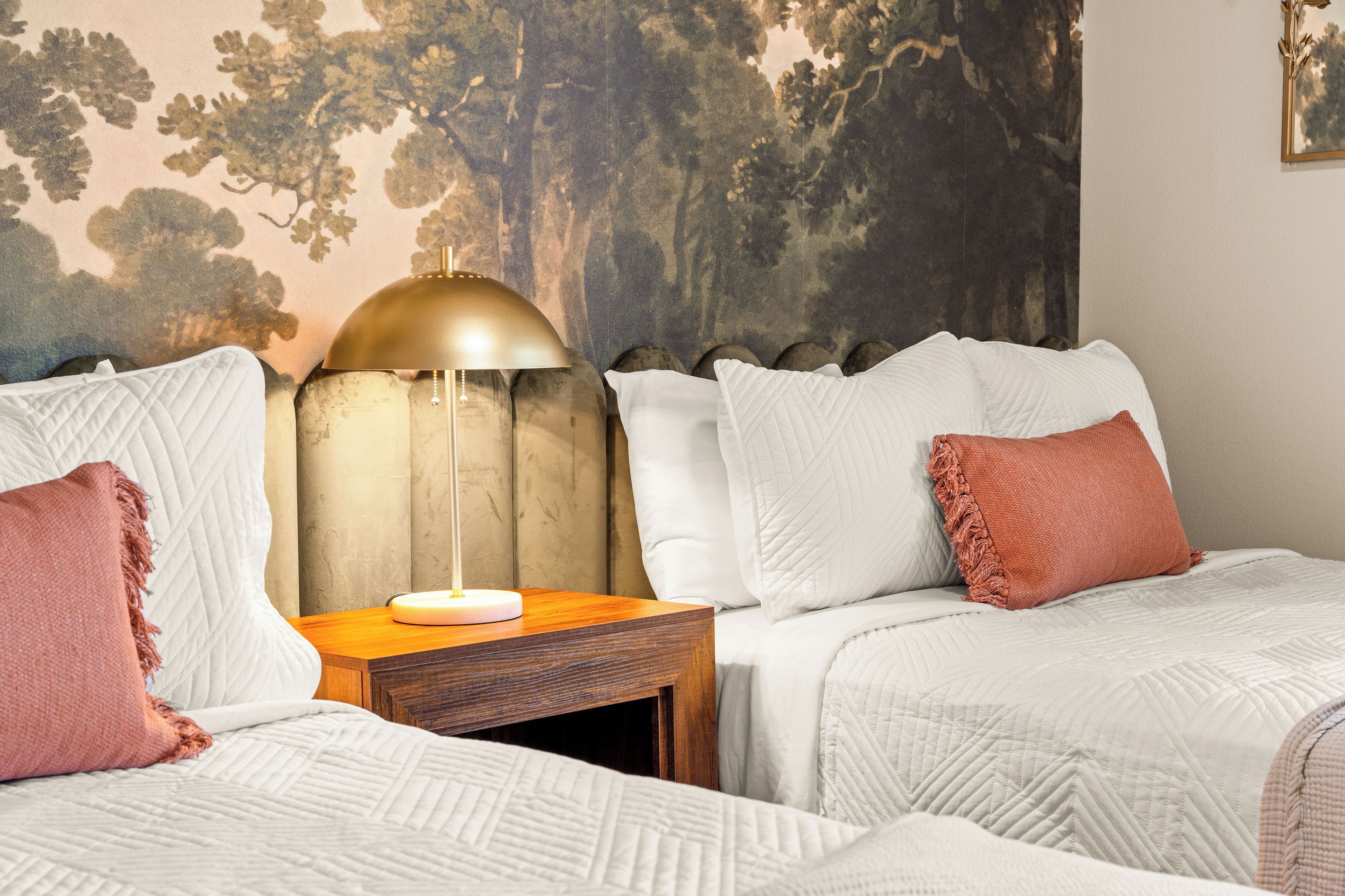 Woodland Bedroom Details
    Soft linens, warm coral accents, and golden bedside lighting complement the dramatic woodland mural, creating a cozy retreat inspired by the beauty of the Ozarks.