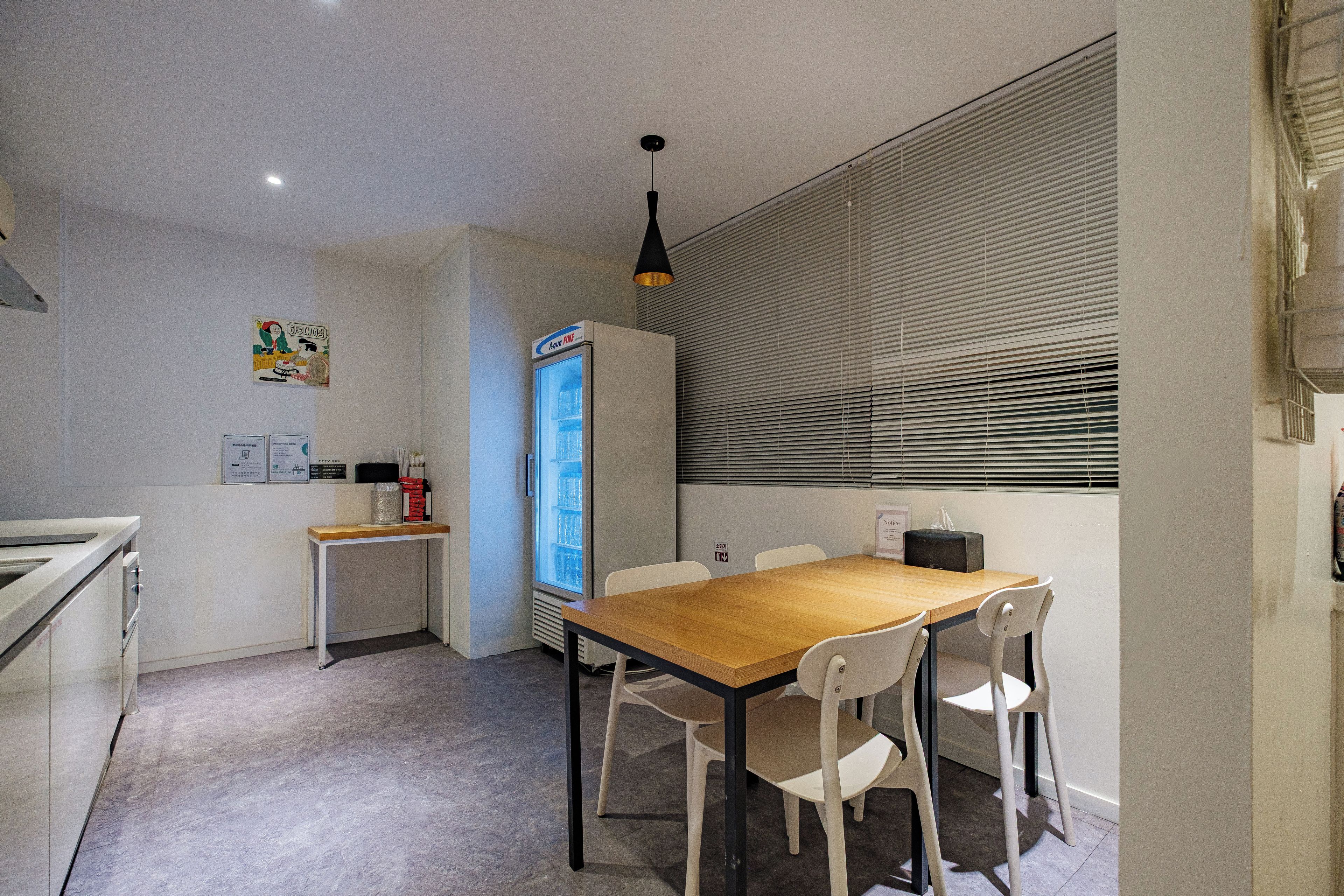 A small, modern kitchen with a dining area, a refrigerator, and a window with blinds.