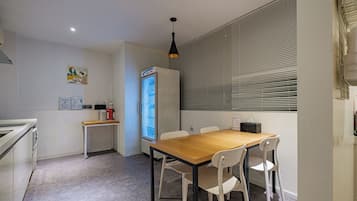 A small, modern kitchen with a dining area, a refrigerator, and a window with blinds.