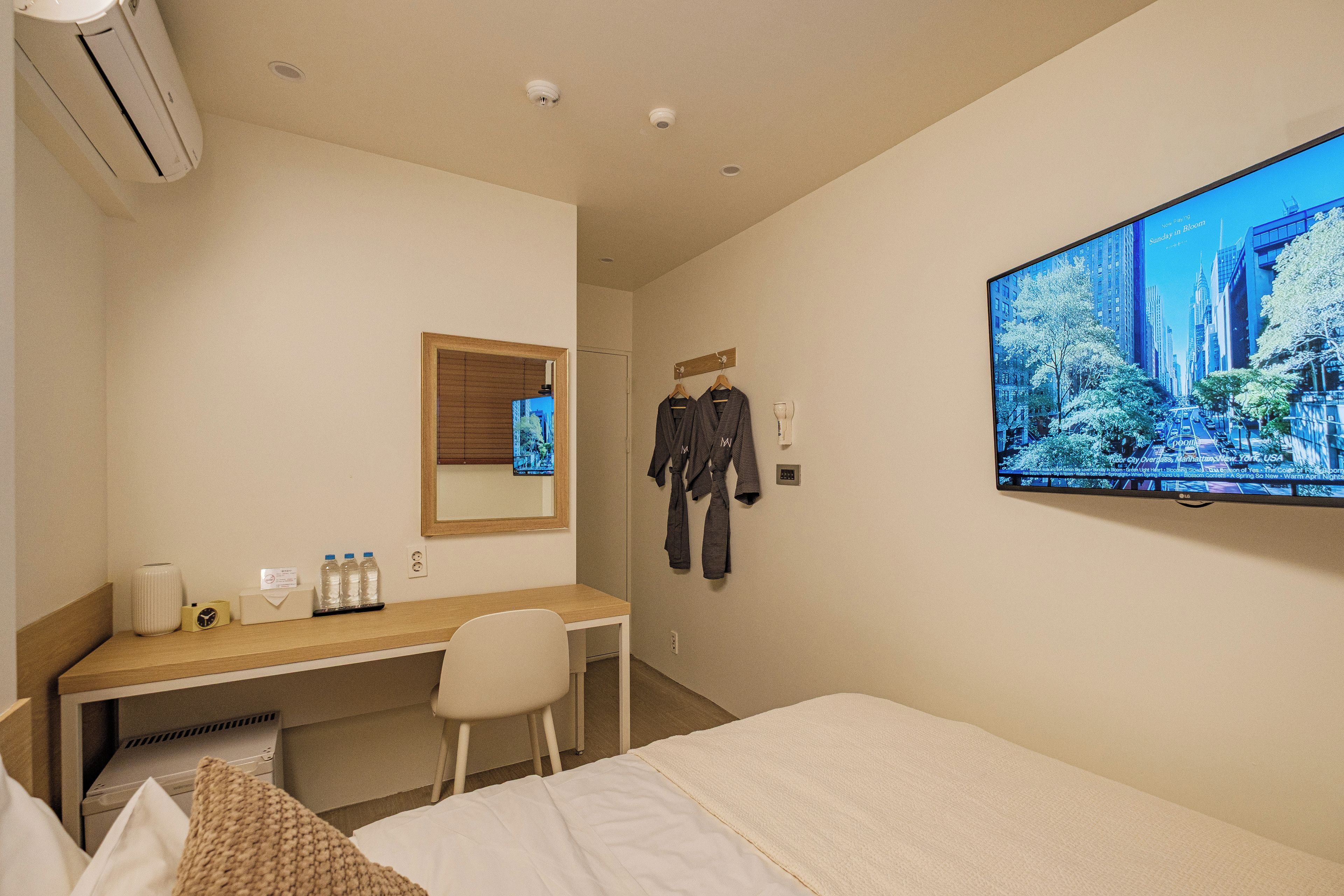 A hotel room with a bed, a desk, a chair, a TV, and a mirror.