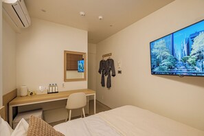 Quarto de hotel com cama, escrivaninha, cadeira, televisão e espelho.