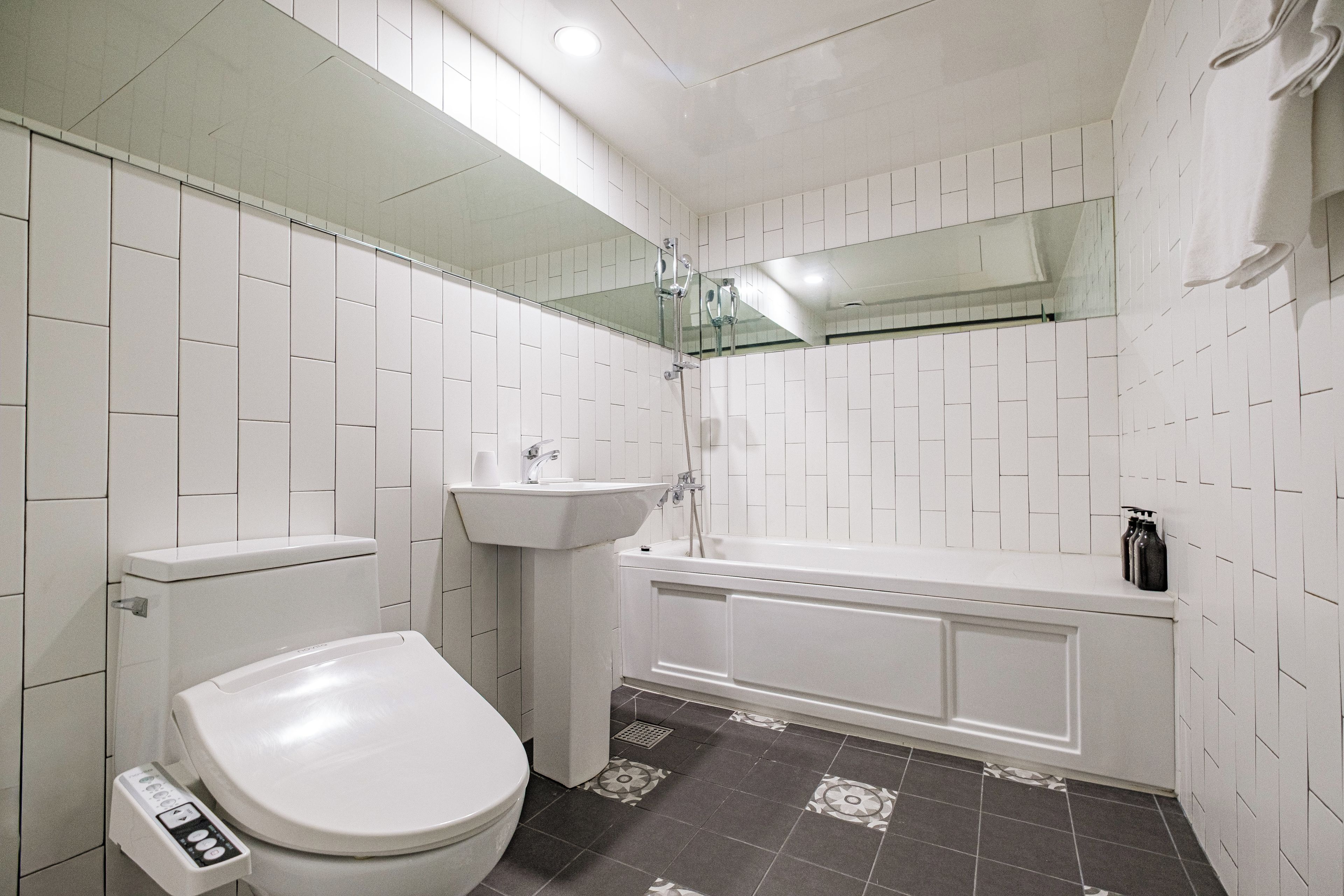 Un bagno con pareti in piastrelle bianche, un WC bianco, un lavandino e una vasca da bagno.