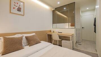 A hotel room with a bed, a desk, a chair, a shower area, and a mirror.