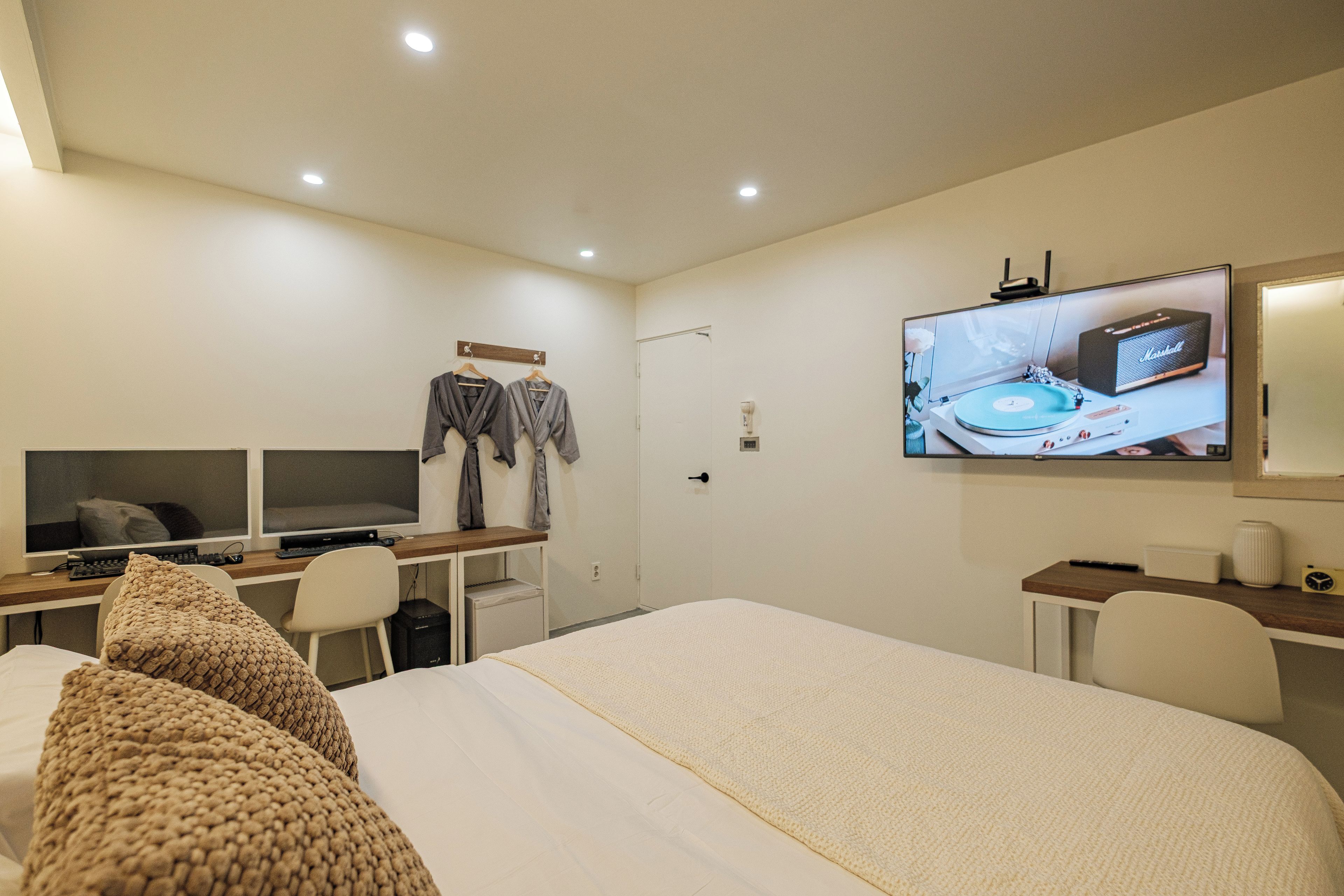 Una habitación de hotel con cama, escritorio con computadora, televisión montada en la pared y armario.