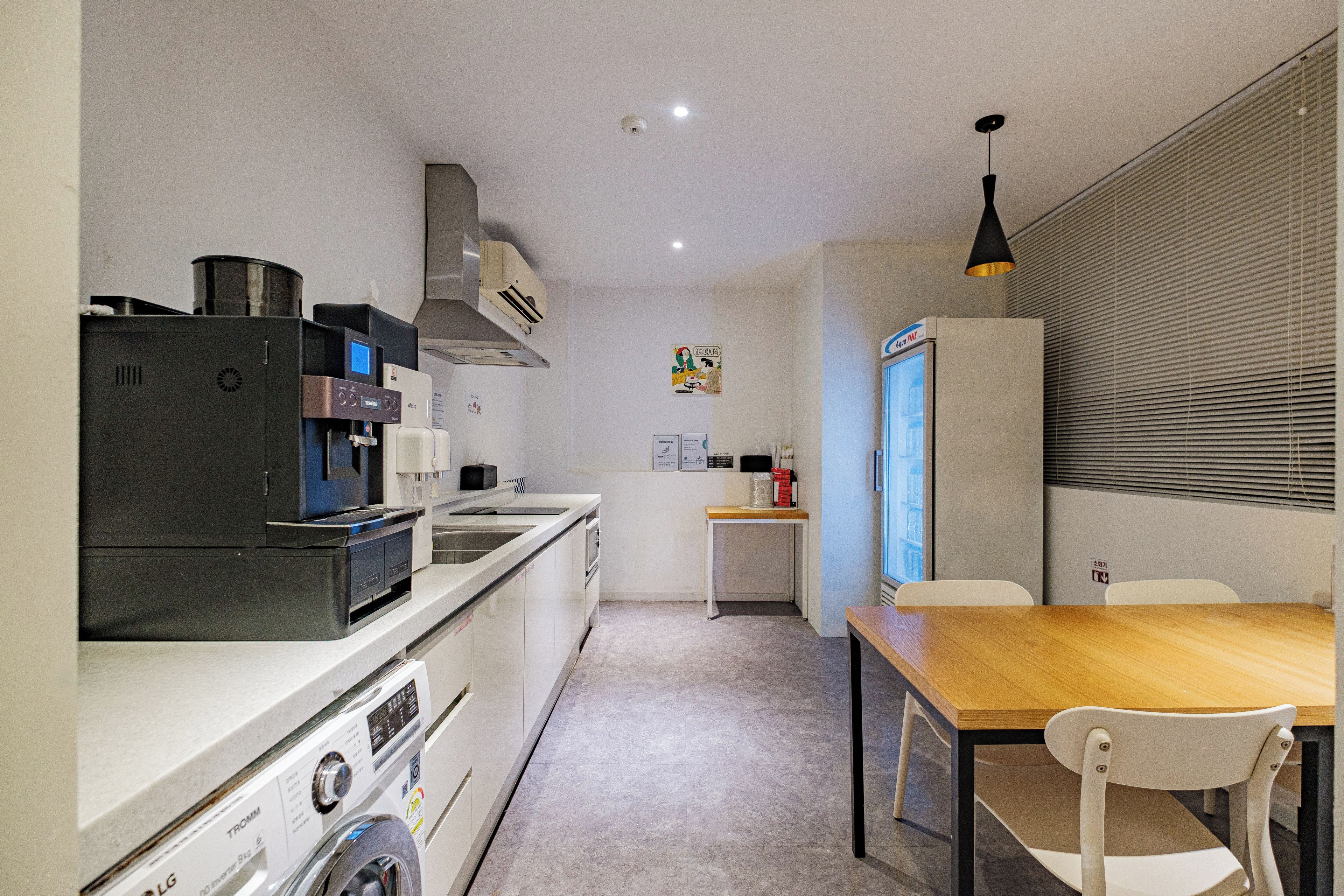 Una cocina compacta con lavadora, cafetera y un pequeño comedor con mesa y sillas.