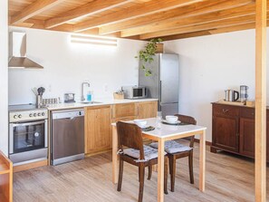 A compact kitchen with wooden cabinets, a dining table with chairs, and a hanging plant. - Secluded Bungalow, Waterfall, Grotto Pool, Cave Plunge Pool, & Sauna (Ponta do Sol)