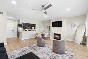A modern living room with a fireplace, a ceiling fan, and a dining area with a kitchen in the background. - Cozy 2-bedroom apartment with AC in welcoming Dallas (Dallas)