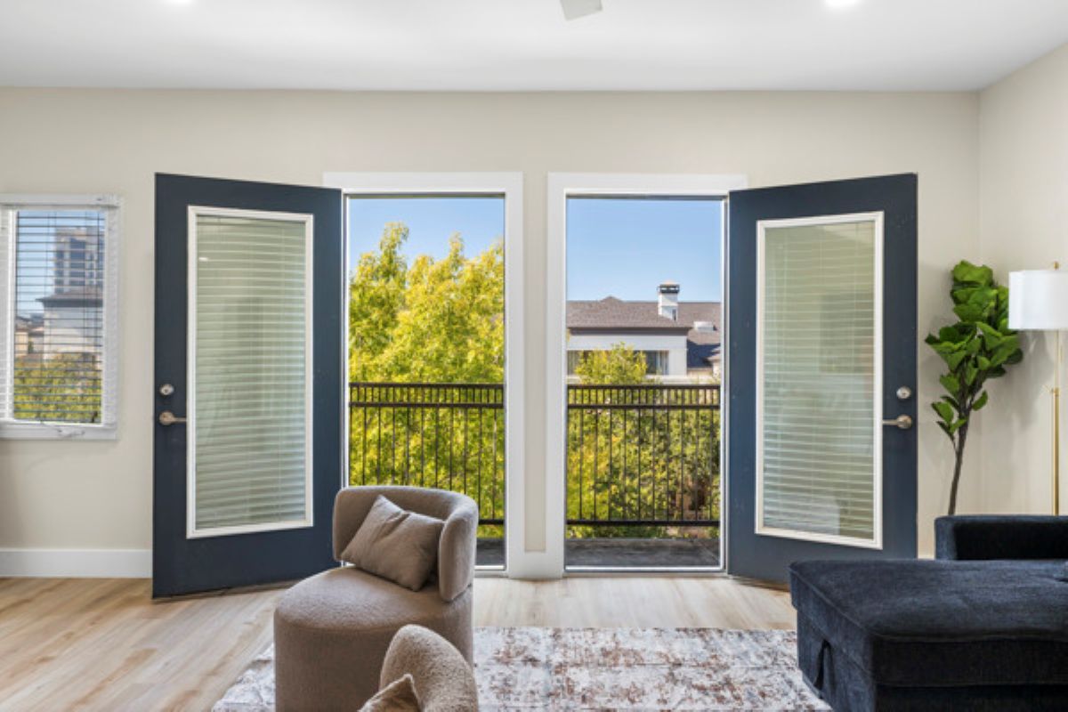 Une pièce comprenant un canapé, un fauteuil, un tapis et donnant sur un balcon par une porte.