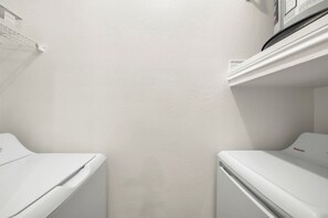 Una sala de bugaderia amb dues rentadores blanques i una estant a la part superior.