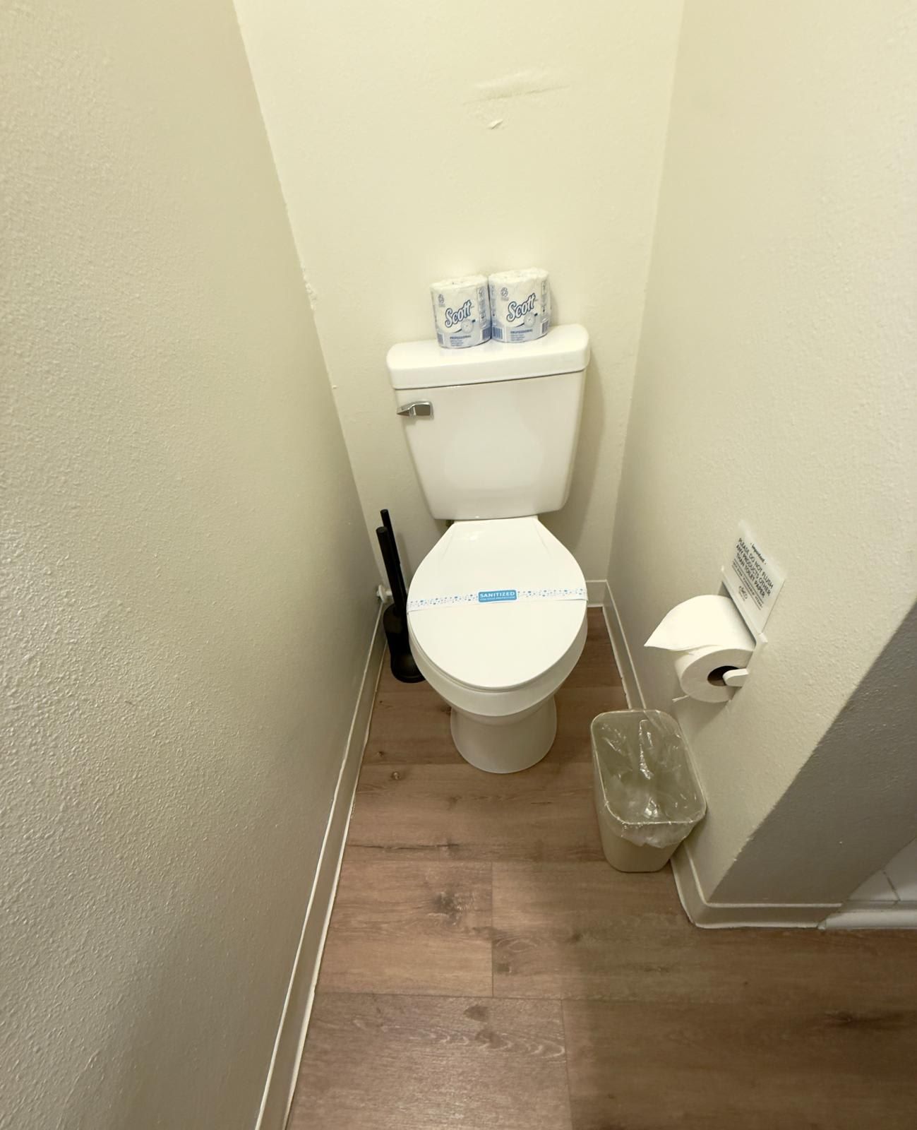 A small bathroom with a toilet, toilet paper, and a trash bin.