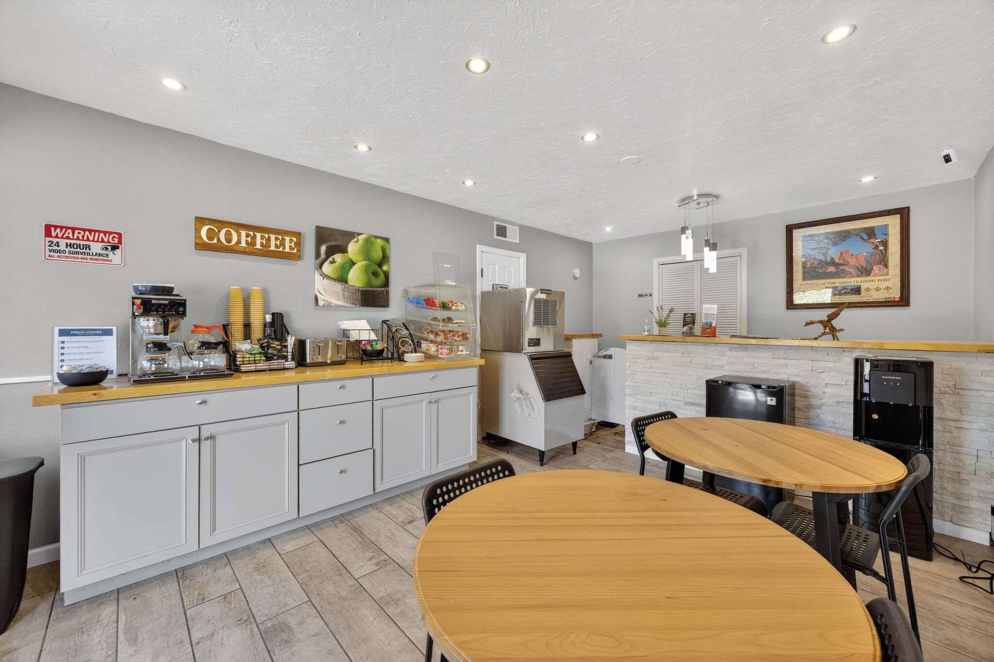A modern kitchen with a coffee station, a dining area with a wooden table, and a refrigerator.