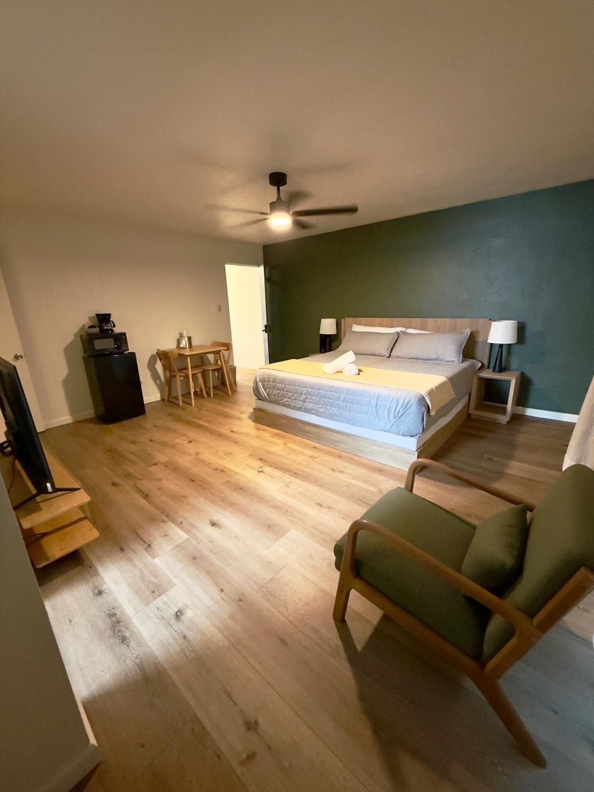 A bedroom with a bed, a desk, a chair, a ceiling fan, and a TV.