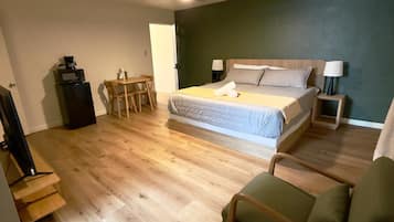 A bedroom with a bed, a desk, a chair, a ceiling fan, and a TV.