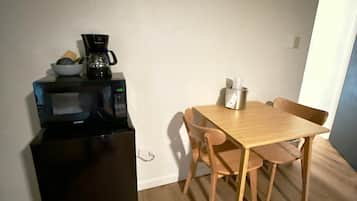 A compact kitchen with a microwave, coffee maker, and a wooden dining table with chairs.
