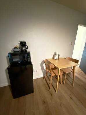 Een kleine keuken met een magnetron, koffiezetapparaat en een houten eettafel met stoelen.
