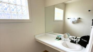 Une salle de bain avec un lavabo blanc, un miroir et une fenêtre donnant sur le ciel.