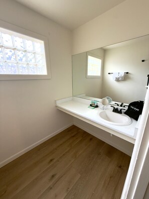 Een badkamer met een wit wastafelmeubel, een spiegel en een raam met uitzicht op de lucht.