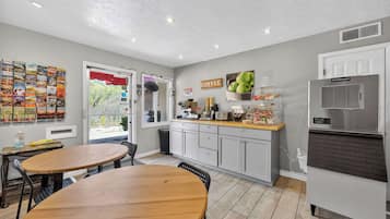 A compact kitchen with a refrigerator, a coffee station, and a dining area with two wooden tables.